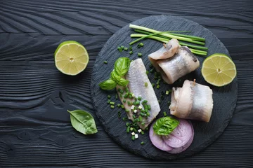 Foto auf Glas Stone slate tray with herring fillet rolls, black wooden surface © Nickola_Che