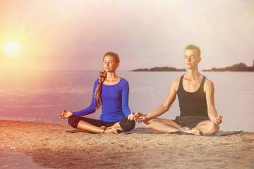 Couple is practicing yoga meditation pose at tropical sunrise