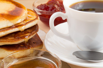 Pancakes with honey, strawberry jam and a cup of coffee close-up