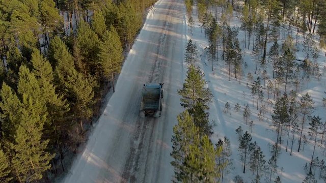 Aerial view of emty truck or lorry going on winter dirt road at background of evergreen forest