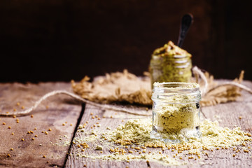 Mustard powder in a glass jar, vintage wooden background, select