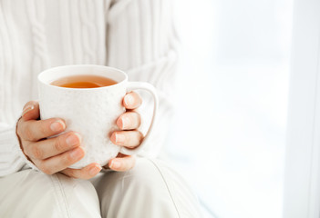  Woman's hands is holding hot cup of coffee or tea in morning su