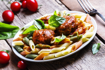 Colorful penne pasta with meatballs in tomato sauce with basil,