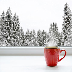 Coffee cup on a window sill. In the background, a beautiful winter forest in snow