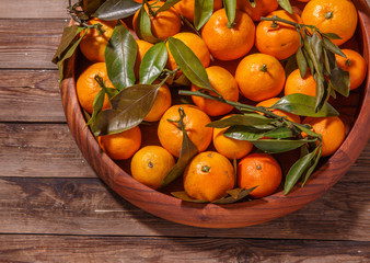 Mandarin oranges with leaves in wooden plate on rustic wood background.