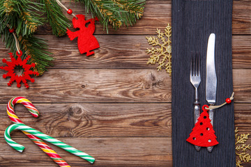Christmas table place setting with fork and knife, decorated christmas toy - red fir-tree, christmas pine branches and two lollipop cane.