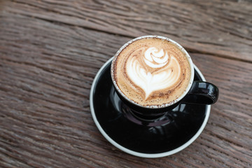 a cup of coffee with latte art in rose pattern on wooden table