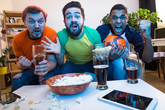 Picture of funny friends watching football game on TV, drinking alcohol drinks and screaming or shouting while catching exciting or amazing moments.