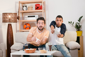 Happy friends playing computer games with help of mobile or smart phones. Handsome friends spending free time all together at home.