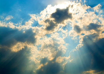 The sun's rays break through the gray clouds, revealing a bright blue sky