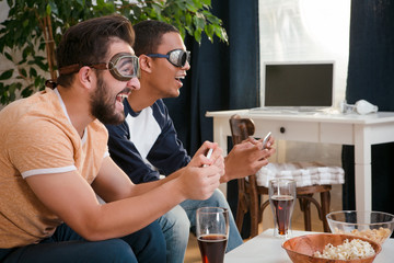 Profile picture of happy friends playing computer games. Handsome men with special 3D glaases on looking at TV screen.