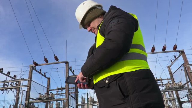 Electrician engineer using tablet near substation and walking away