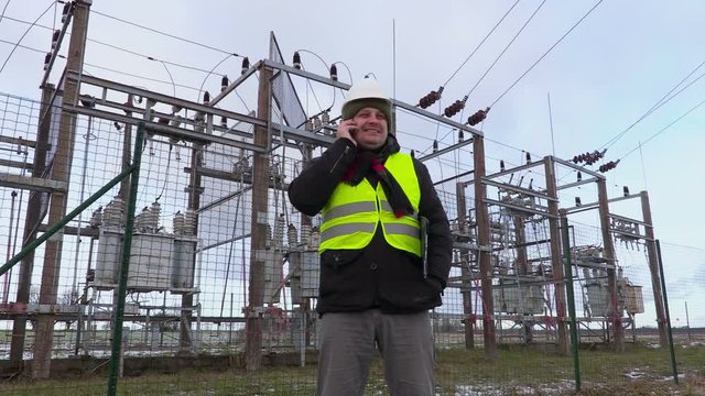 Electrician engineer talking on smart phone near substation in winter