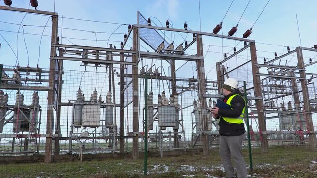Electrician engineer writing and walking near substation in winter
