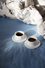 Two white cups of coffee are in bed, sunny morning
