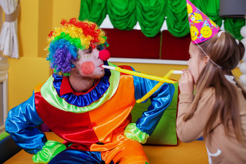 Clown and girl plays with tube on birthday party.