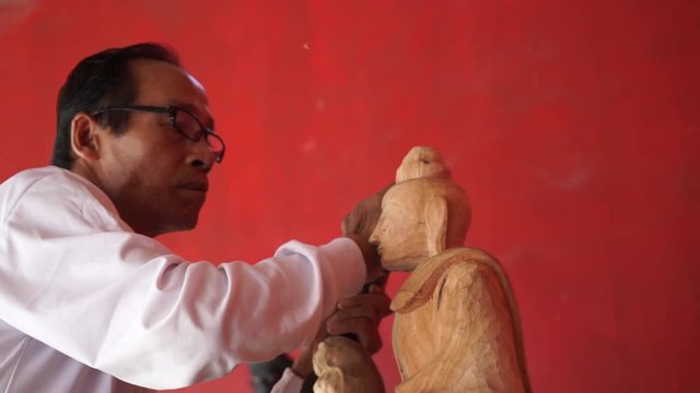 Man carves a statue of Buddha made of wood