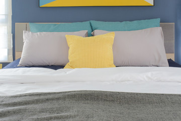 Yellow, gray and turquoise color pillows setting on bed in bedroom