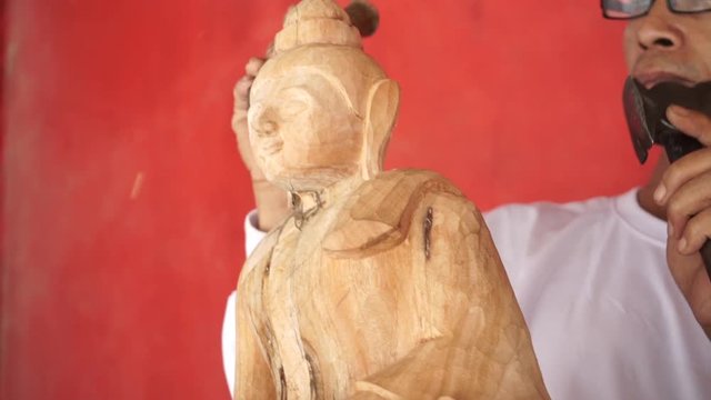 Man carves a statue of Buddha made of wood