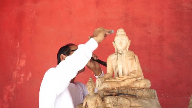 Man carves a statue of Buddha made of wood