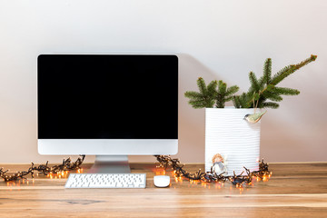 Modern workspace. Computer on a wooden walnut table. A vase with a fir branch and garland for christmas mood. 