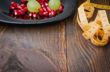 centimeter, pomegranate and grapes in a plate on a fitness background/centimeter, pomegranate and grapes in a plate on a wooden background