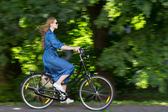 Beautiful young woman and vintage bicycle, summer. Red hair girl riding the old black retro bike outside in the park. Having fun in the city