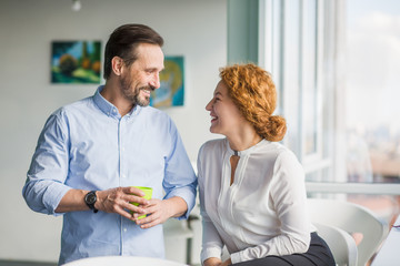 Businessman and businesswoman communicating during break time of their work. Man drinking coffee or tea and looking at his colleague in office interior.