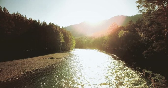 4k (UHD) aerial view. Low flight over fresh cold mountain river at sunny summer morning. Green trees and sun rays on horisont.
