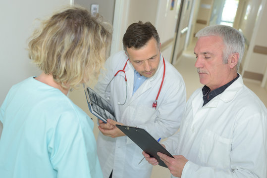 two doctors and nurse looking at clipboard in hospital