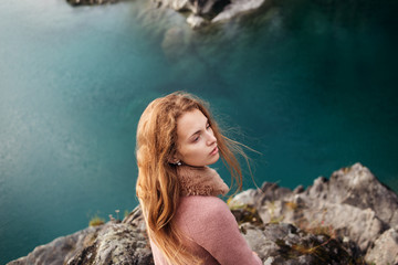 Girl in pink coat standing on a promontory above the lake