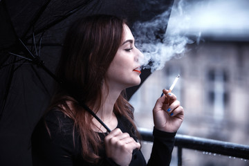 young woman holding an umbrella and smoking a cigarette