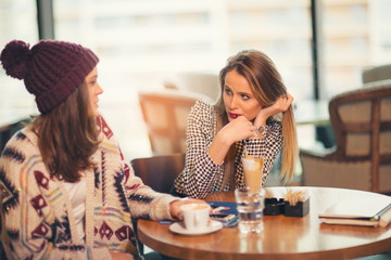 Two friends enjoying coffee together in a coffee shop as they sit at a table chatting