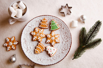 Beautiful Christmas background with gingerbread cookies on a white plate with a branch of a tree and forms for cookies