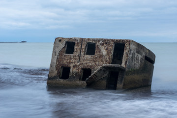 Naklejka premium Liepaja beach bunker. Brick house, soft water, waves and rocks. Abandoned military ruins facilities in a stormy sea. Barracks building in the Baltic sea. Liepaja, Latvia, Europe.