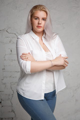 Portrait of a pretty big blonde in a white shirt on a gray background.