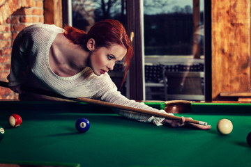 Young attractive woman plays the game of snooker pool table. Fun and competition concept