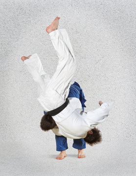 Two judokas fighters fighting men on gray