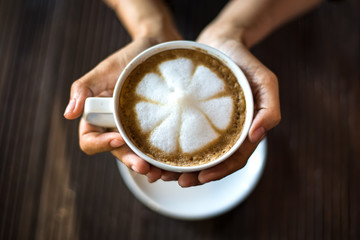 Hands holding hot cup of coffee or tea in morning sunlight
