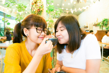 Smiling female asian friends holding coffee mugs while talking b