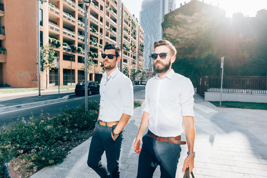 two young bearded blonde and black hair modern businessman, walking in the city backlight,talking together - working, successful concept