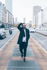 Half length of young handsome caucasian bearded businessman walking outdoor in the street, overlooking pensive wearing sunglasses - business, thoughtful, serious concept