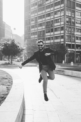 Young handsome contemporary business man jumping outdoor in city back light - success, positive, winner concept - black and white