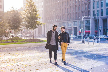 Two young bearded blonde and black hair modern businessman, walking in the city using smart phone - working, successful concept