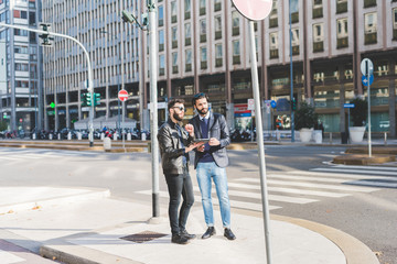 two young bearded modern businessman using tablet handhold outdoor in the city, discussing - technology, business, work concept