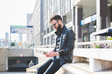 young contemporary businessman leaning on wall outdoor in the city holding a smartphone - technology, social network, communication concept
