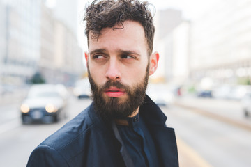 Portrait of young handsome caucasian bearded businessman posing outdoor in the street, overlooking pensive - business, thoughtful, serious concept