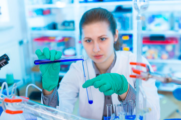 Attractive young female scientist working in laboratory.  Woman scientist looking at a red test tube in a lab