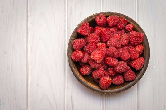 Raspberry in bowl on white  wooden  background. Top view. Organic food.