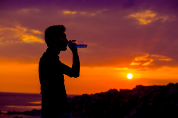 Profile of man silhouette drinking water from a bottle at sunset with the sun in the background